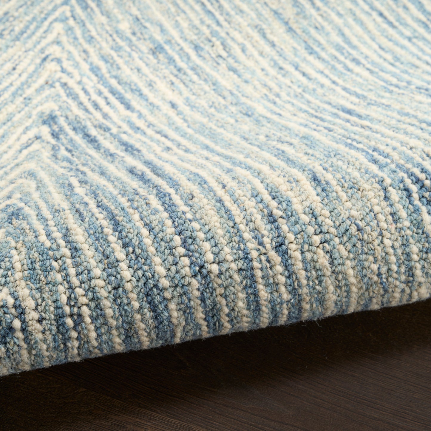 Blue and ivory loop-pile rug with subtle striped gradient and plush texture on dark wood floor.