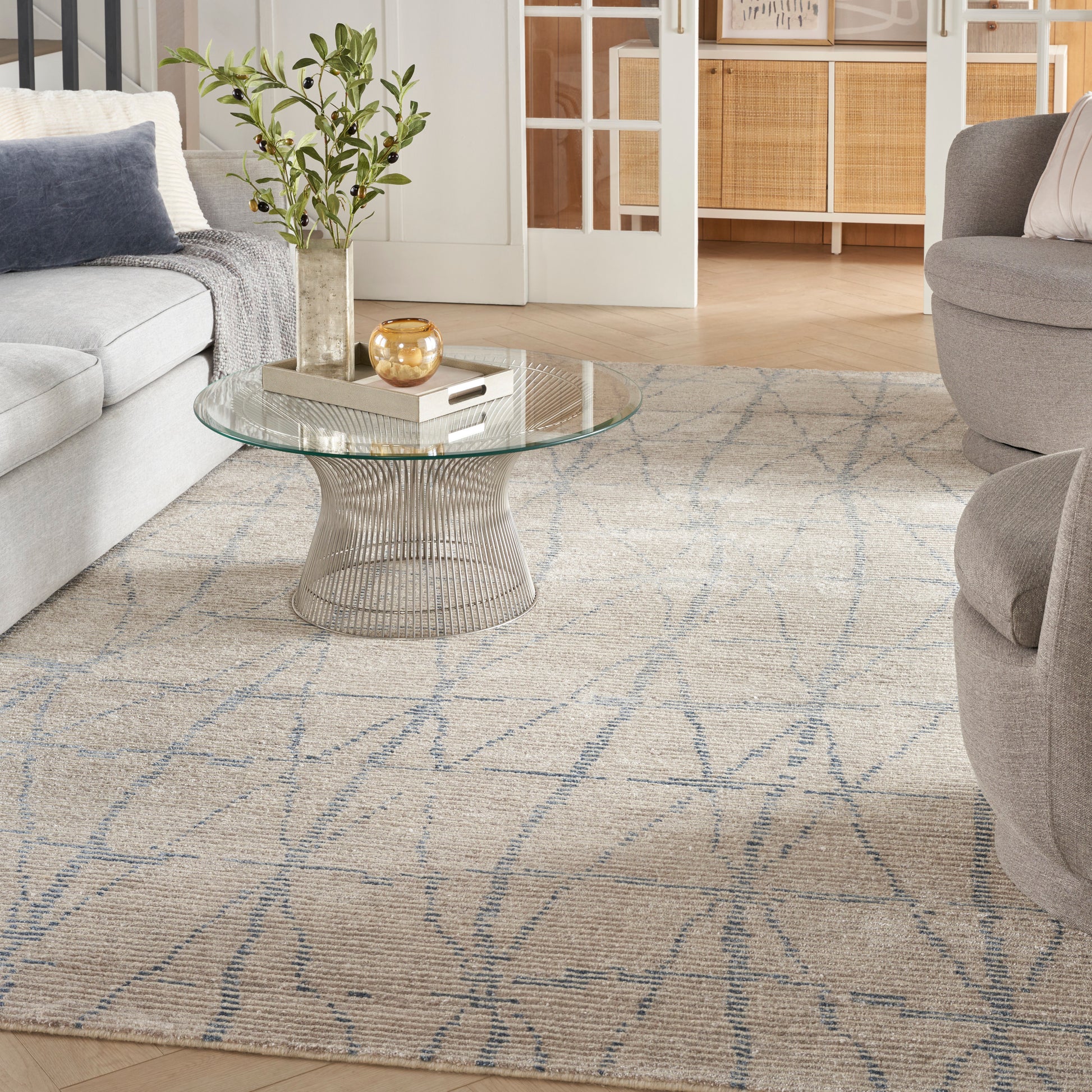 Beige patterned Scandinavian rug, 9' x 12', placed in a modern living room with gray sofas and a plant.