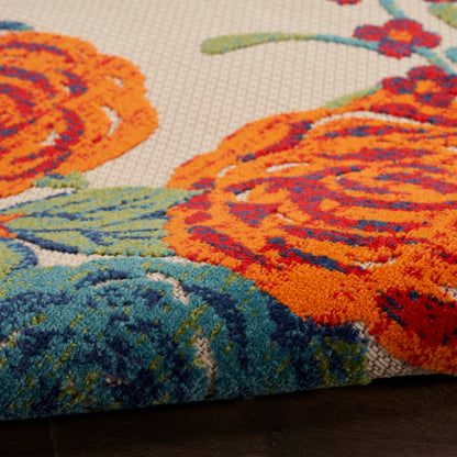 Close-up of an outdoor floral rug: bright orange flowers with teal-green leaves on a beige textured pile.