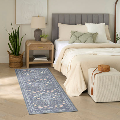 Neutral bedroom with grey tufted headboard, beige bedding, wood nightstand, potted plant, and blue floral runner rug.