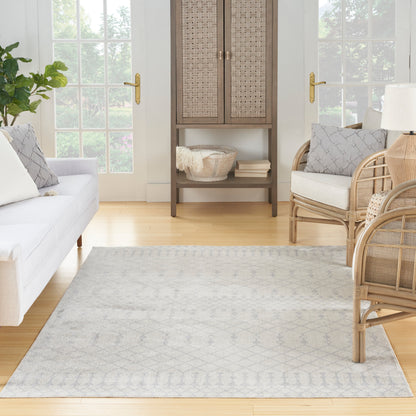 Light gray geometric area rug on warm wood floor in airy living room with white sofa, wicker chairs, and woven cabinet.