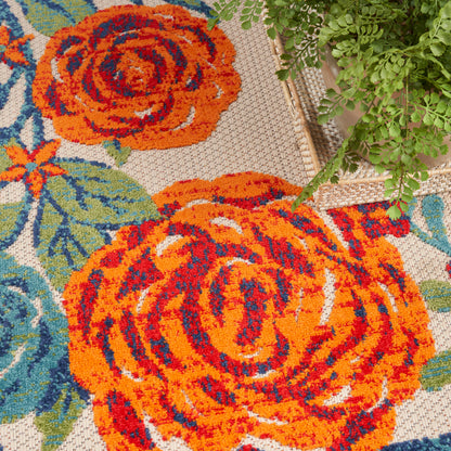 Bright orange rose-pattern rug with teal leaves on a beige background; trailing green plant at the edge.