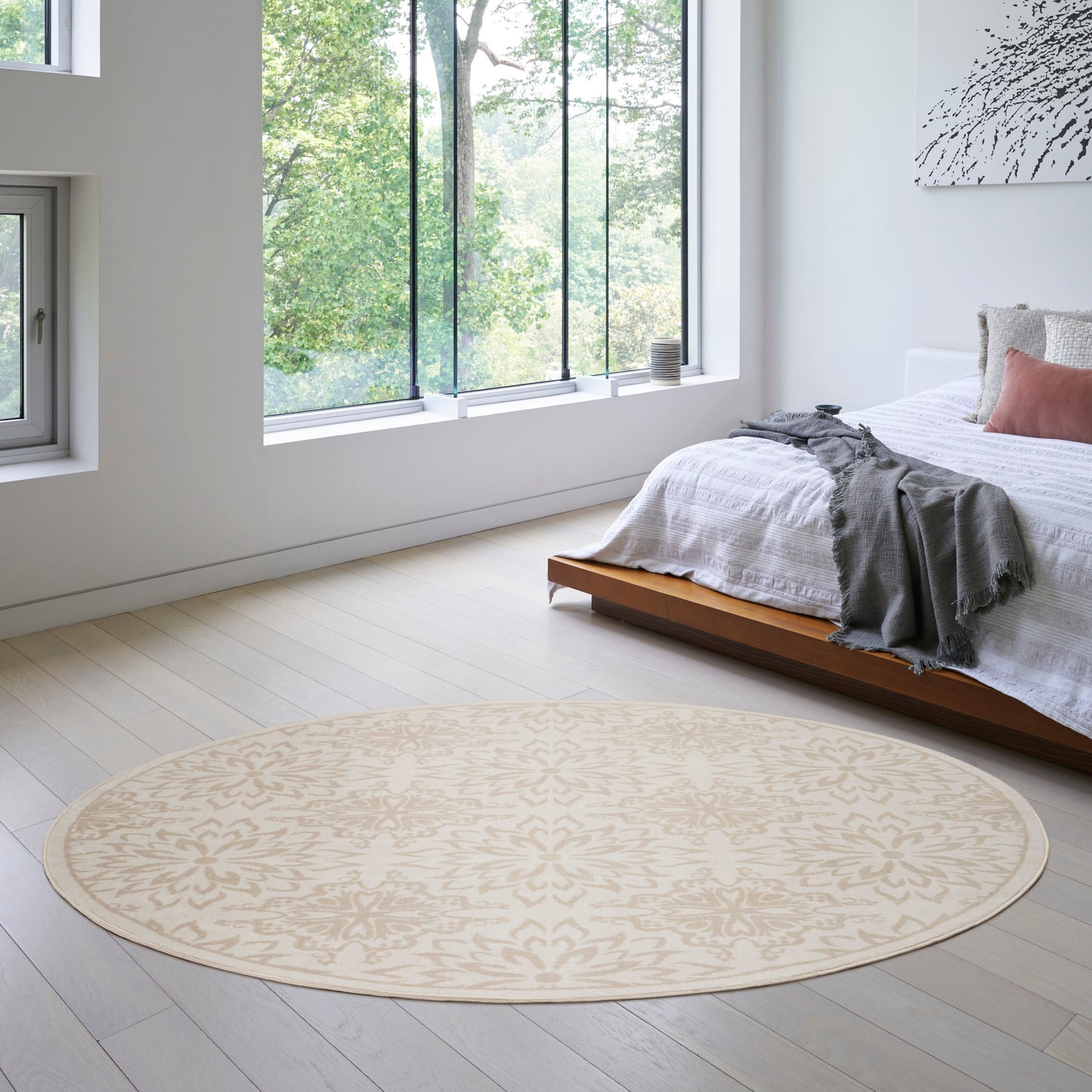 Beige round rug with a subtle pattern in a bright modern bedroom with a low wooden bed and white linens.