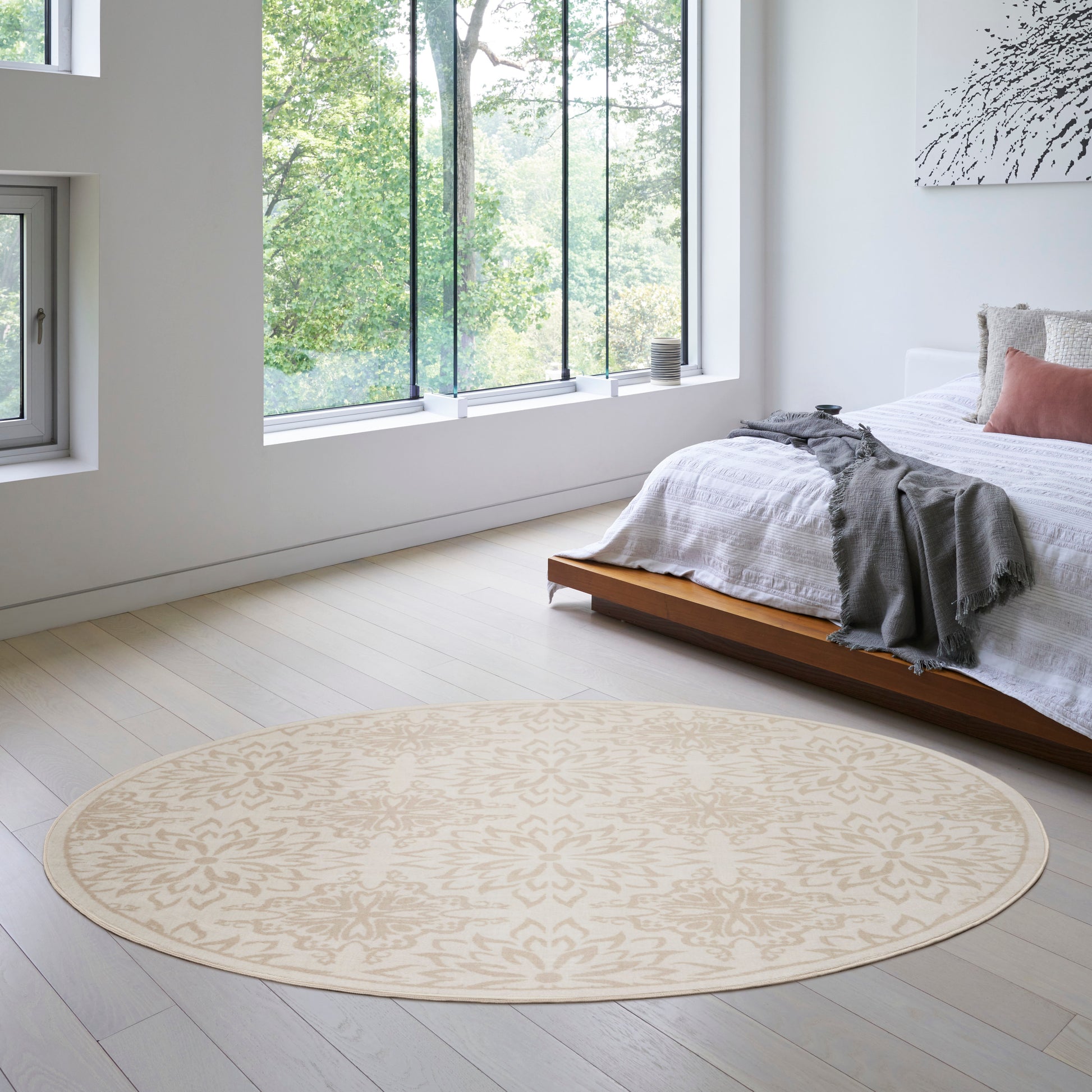 Beige round rug with a subtle pattern in a bright modern bedroom with a low wooden bed and white linens.