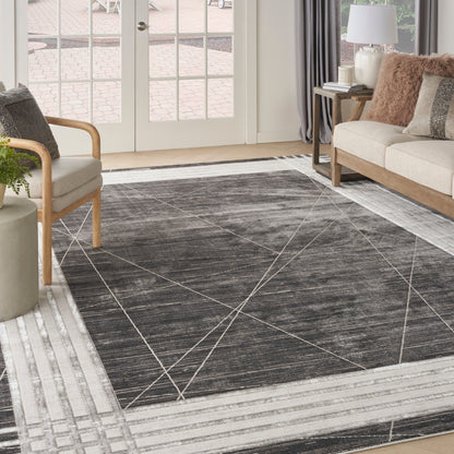 Dark gray geometric area rug with white lines and light striped border in a bright living room with beige sofa and chair.