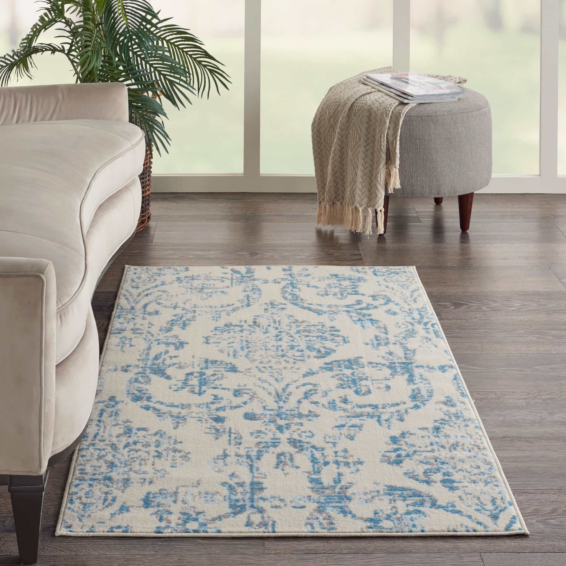 Cream and blue patterned area rug on dark wood floor in a bright living room with a beige sofa and round gray ottoman.