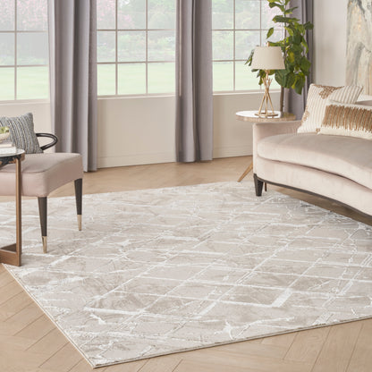 Neutral living room with beige sofa, light gray geometric rug, wood floors, gray drapes, round side table, lamp and plant.