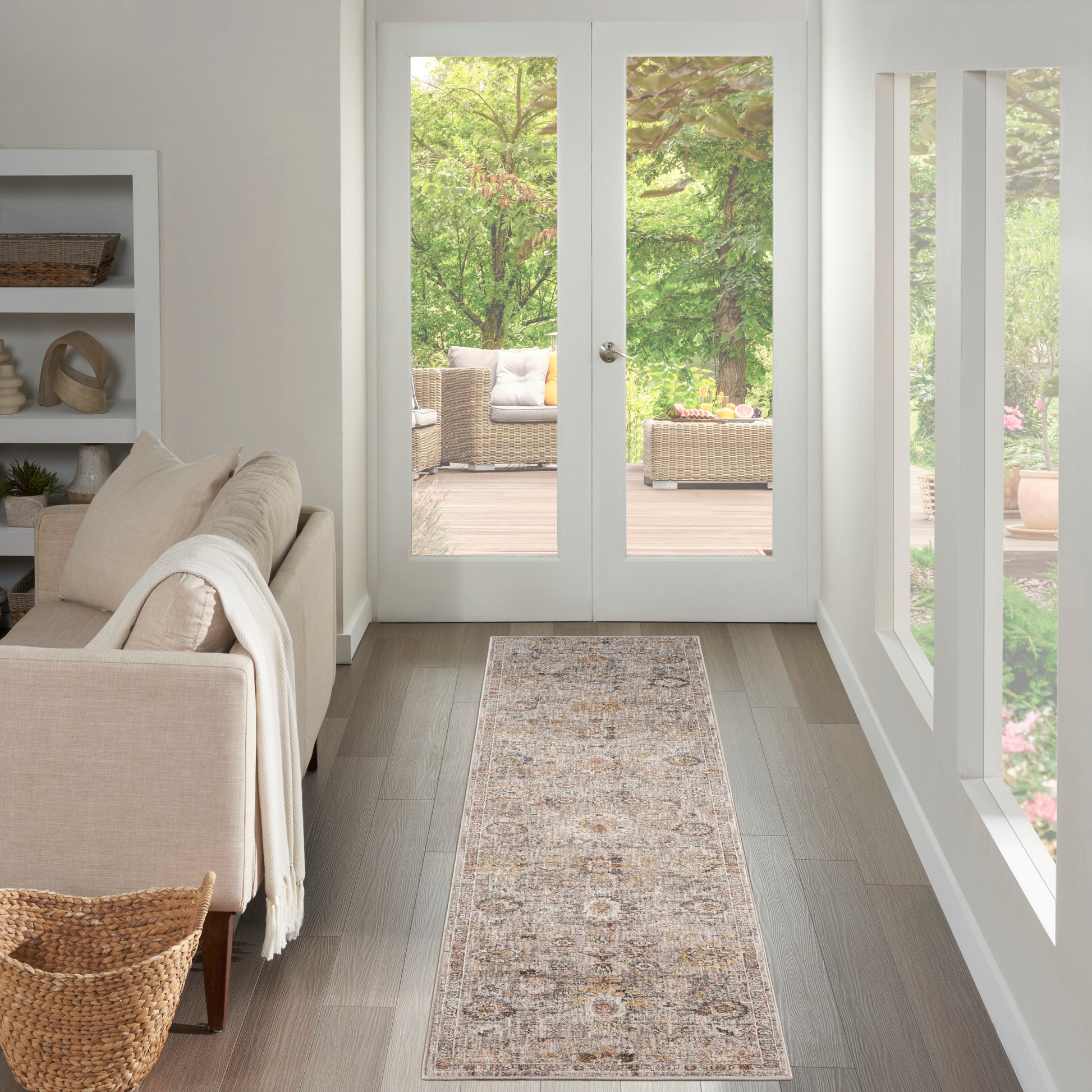 Cozy living room hallway with beige sofa, throw blanket, built-in shelves, and a patterned rug leading to glass doors.