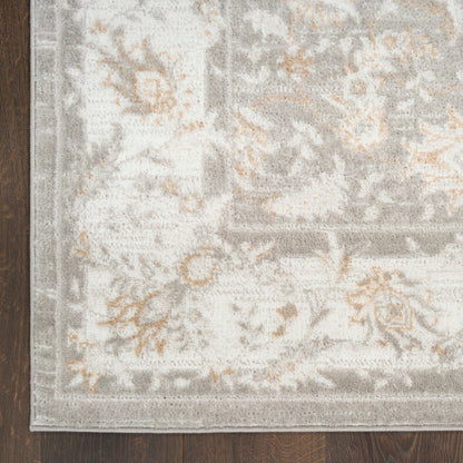 Soft gray and ivory ornate rug with subtle tan floral accents and a decorative border on dark wood floor.