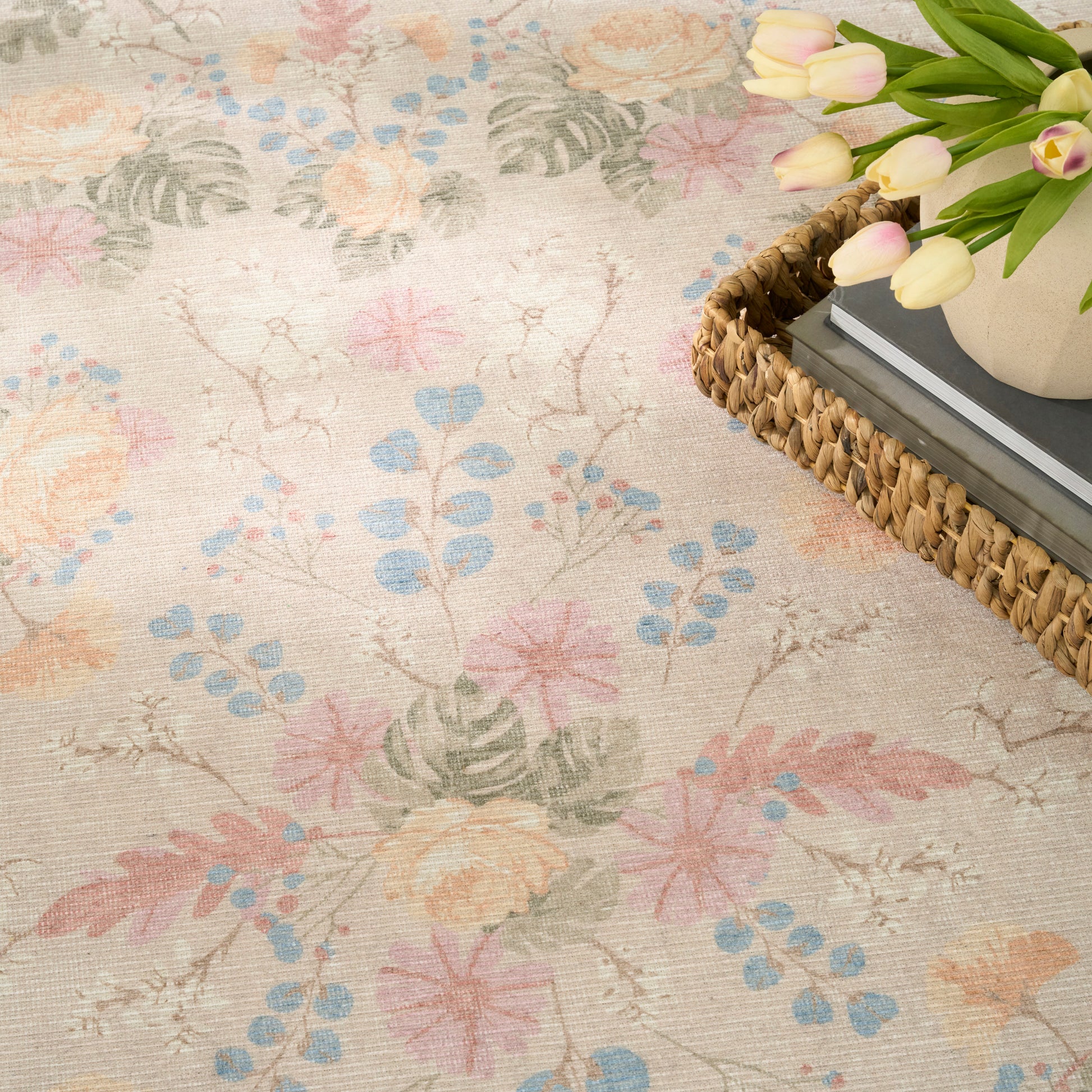 Pastel floral area rug with pink, blue, yellow blossoms; woven basket with books and tulips on corner.