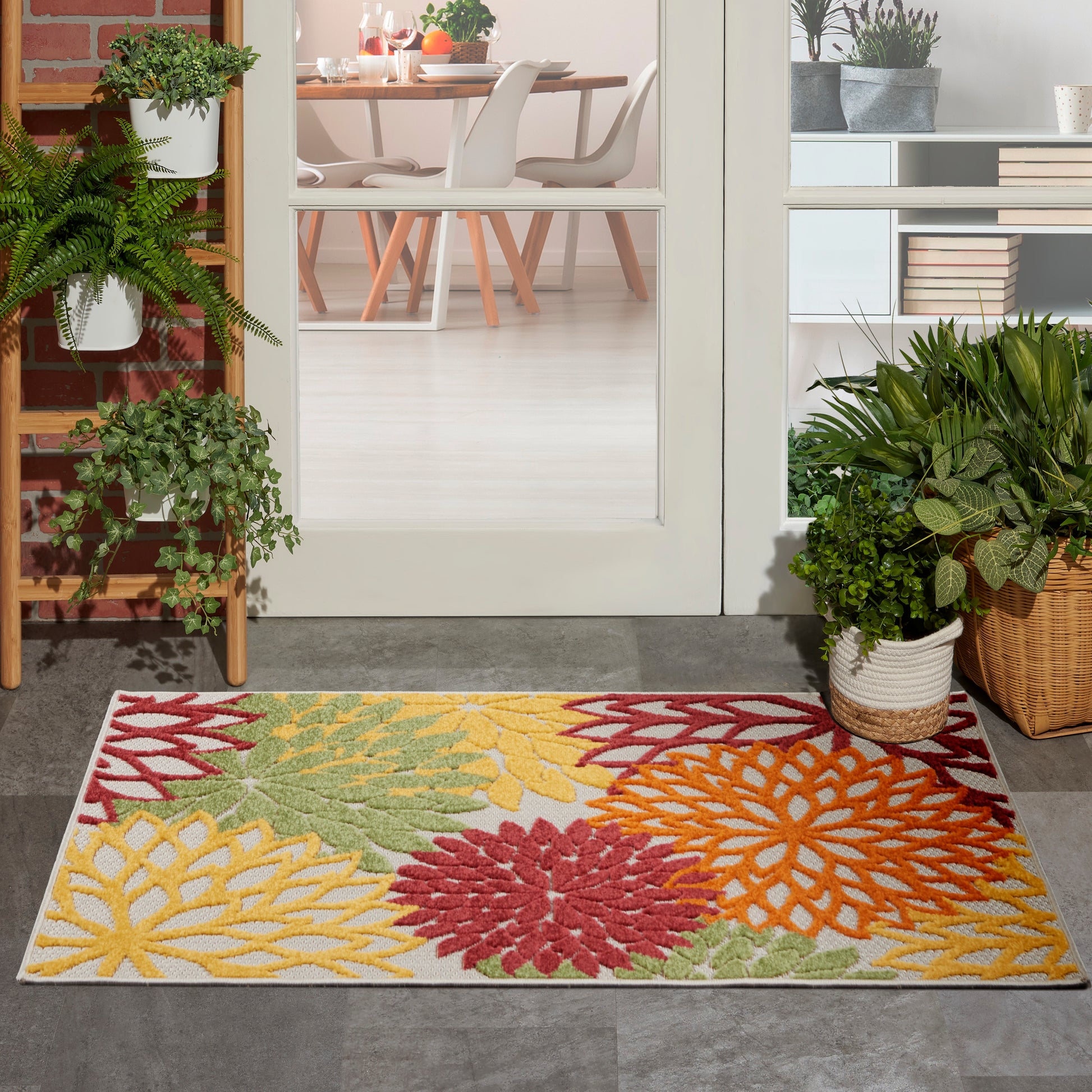 Colorful floral area rug with large yellow, green, red & orange petals, placed at entry with potted plants & glass doors.