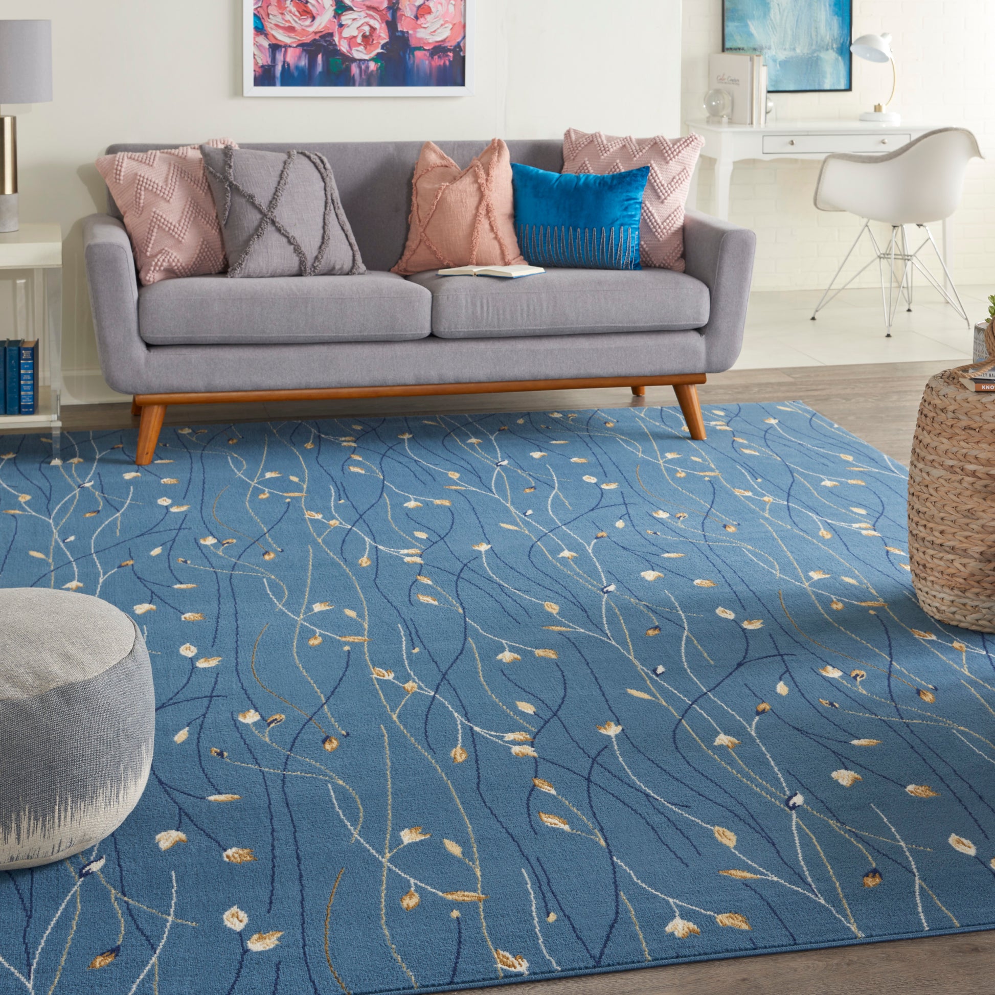 Blue area rug with wavy lines & small leaf motifs under a gray mid-century sofa with pink & blue cushions.