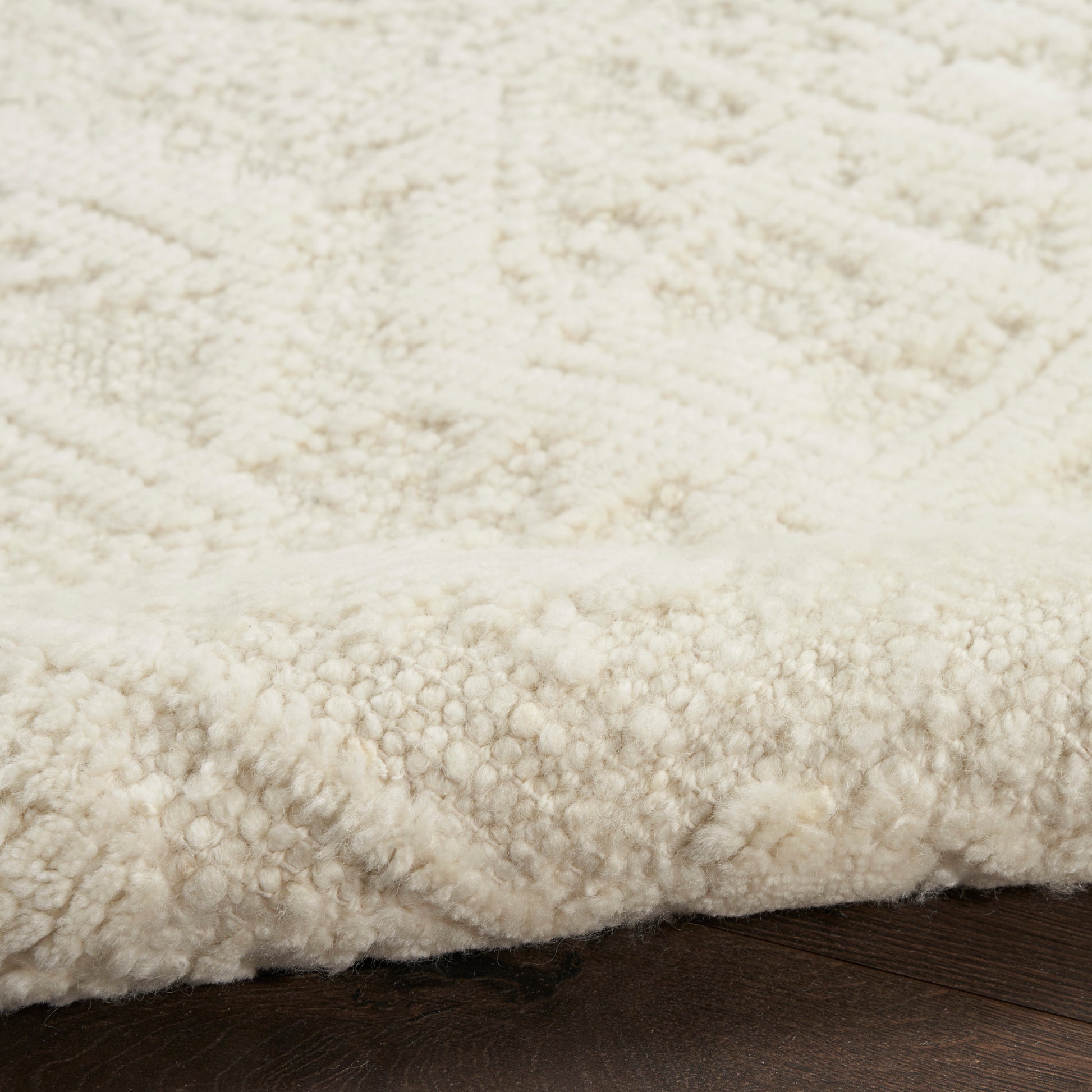 Cream shaggy rug with thick plush pile and textured loops on a dark wooden floor.
