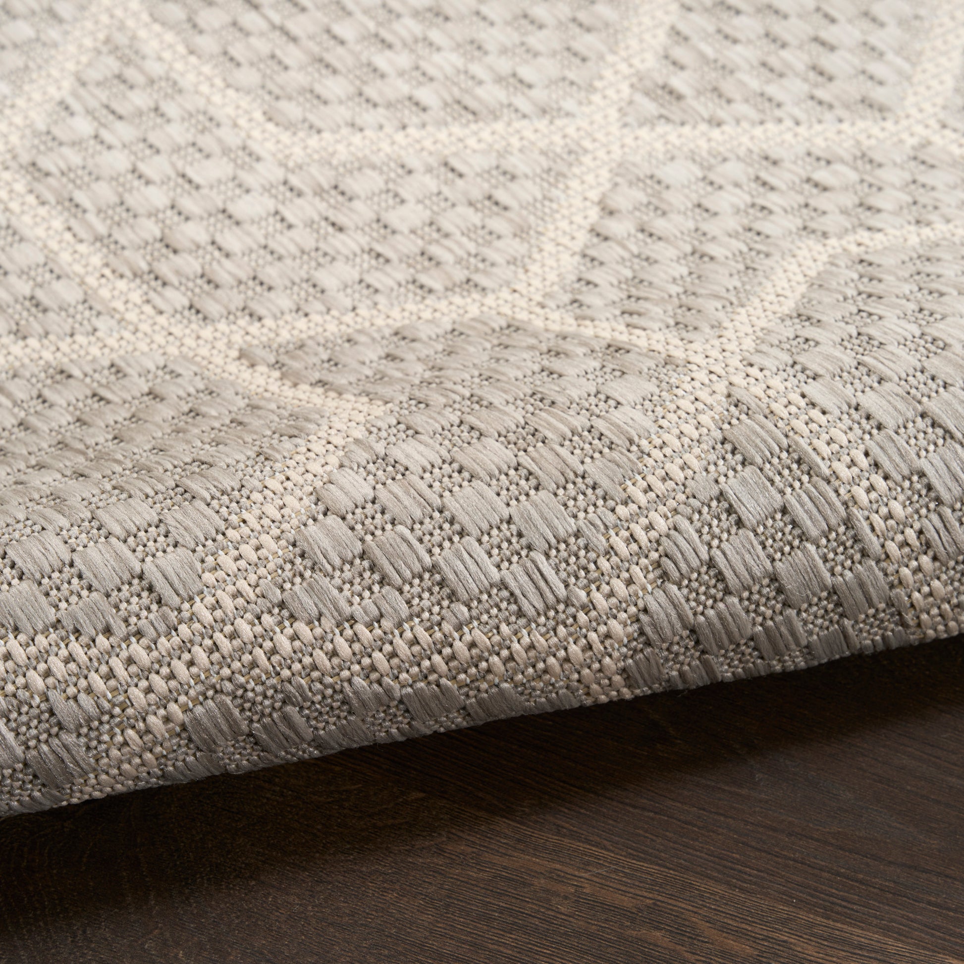 Neutral gray-beige woven rug with raised geometric pattern and textured loop weave on dark wood floor.