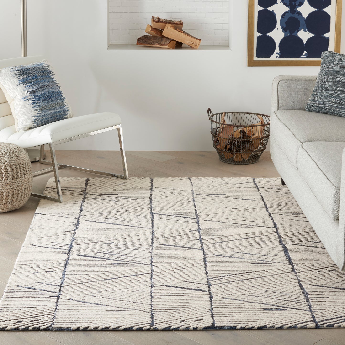Cream geometric rug with navy lines in a modern living room; light gray sofa, white chair, woven pouf, log basket.