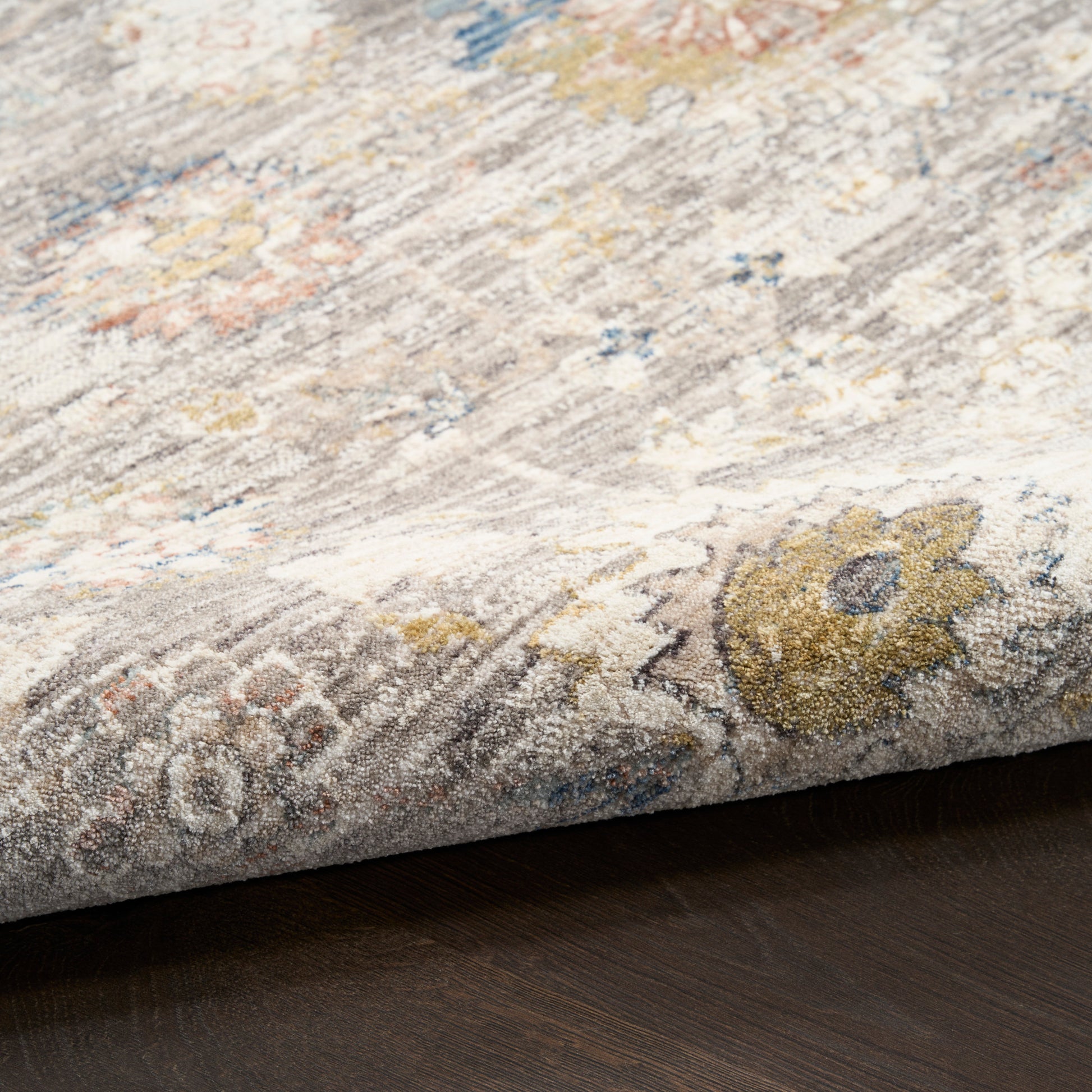 Rectangular vintage-style floral area rug with muted beige-gray tones, gold accents and blue highlights; woven texture.