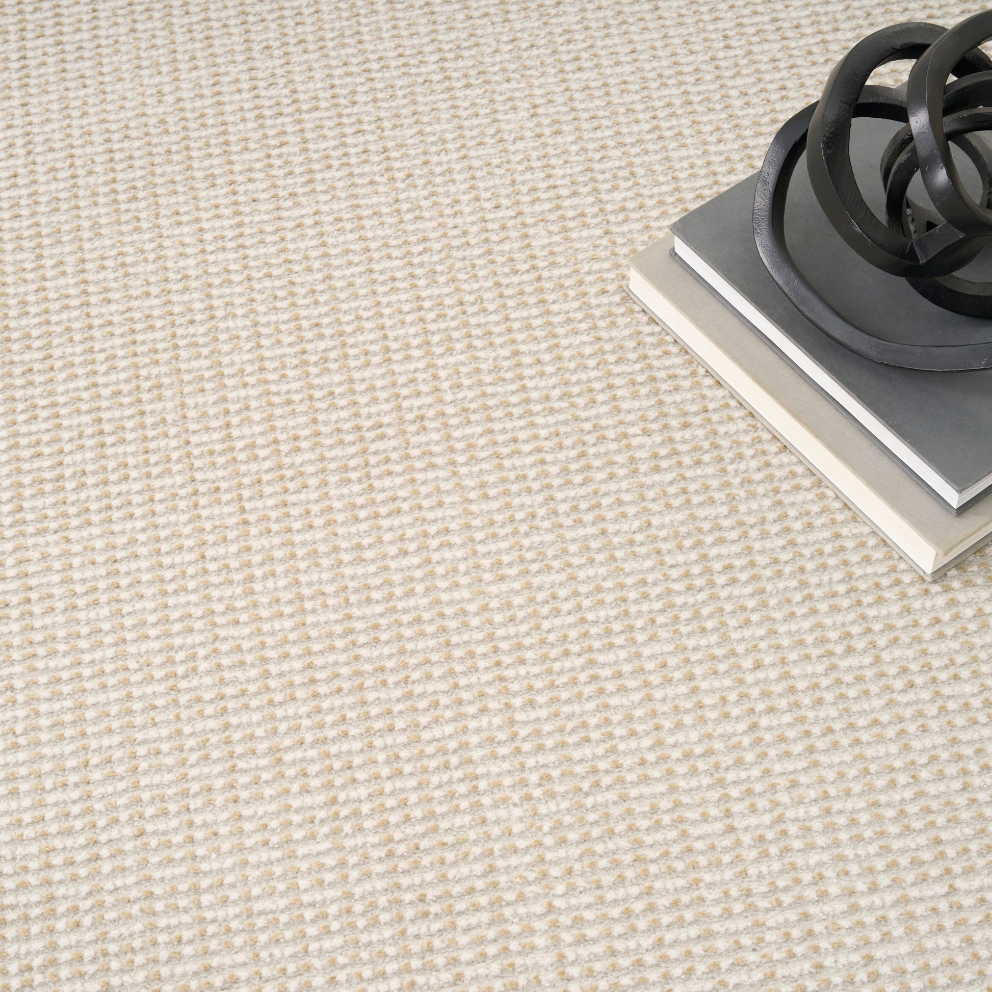 Beige textured carpet with a stack of gray and white books topped by a black circular metal sculpture.
