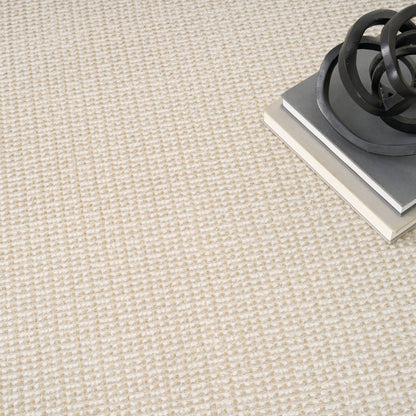 Beige textured carpet with a stack of gray and white books topped by a black circular metal sculpture.