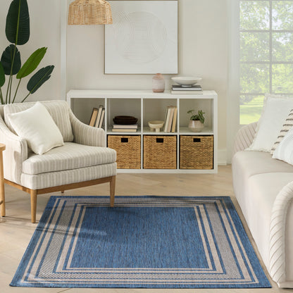 Bright living room with beige striped armchair, white sofa, blue bordered rug, and white cubby shelving with wicker baskets.