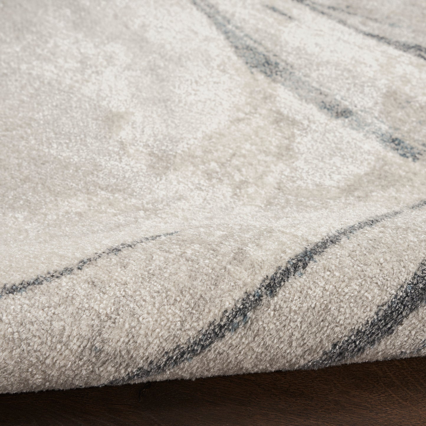 Beige plush rug with dark gray abstract wavy lines, soft pile, resting on a wooden floor.