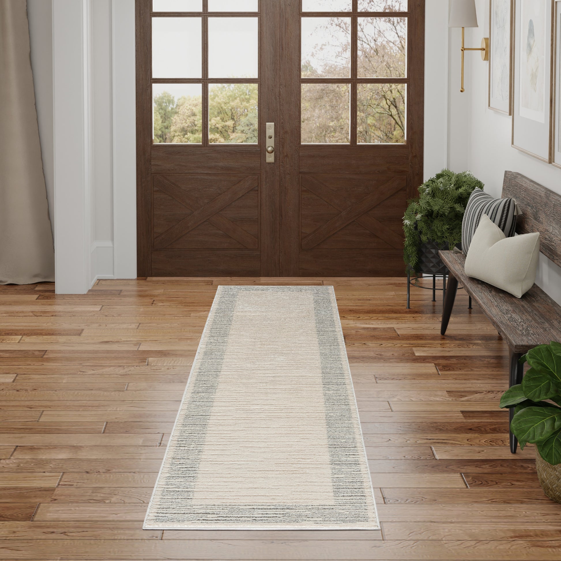 Beige runner rug with subtle gray border on hardwood entryway; double wooden doors, bench with cushions, and plants.