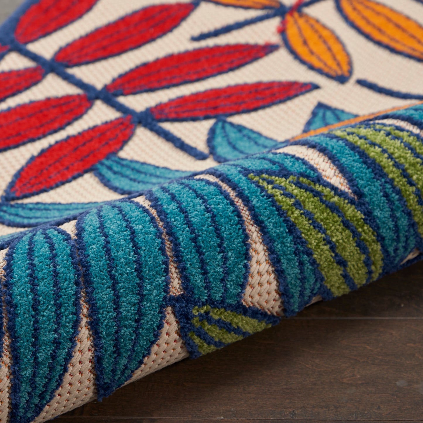 Rolled woven rug with red leaf pattern on beige field and teal-blue striped border.