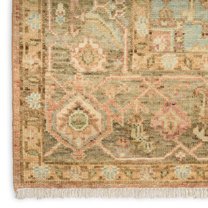 Geometric Persian-style rug corner with beige base, pink, blue and green motifs, fringed edge.