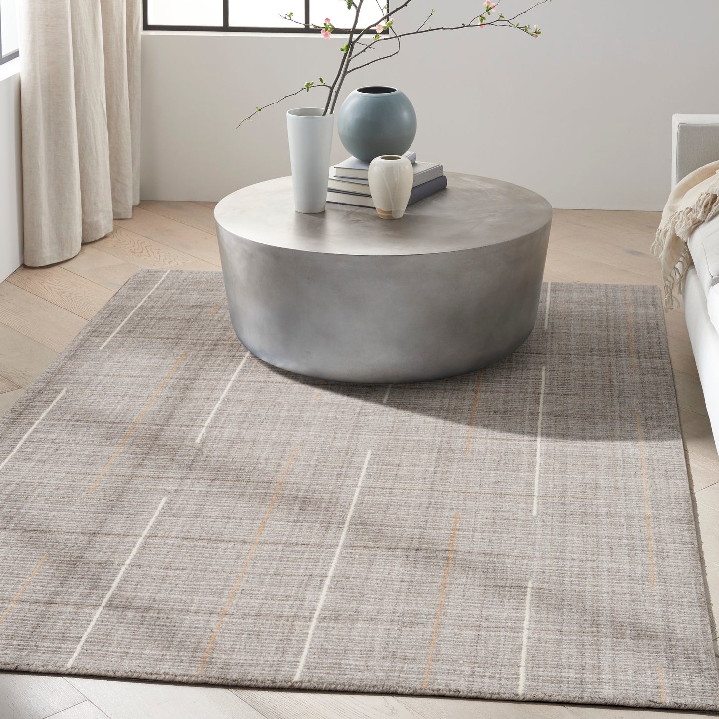 Round concrete-look coffee table with blue and white vases and books on a gray plaid rug in a bright modern living room.