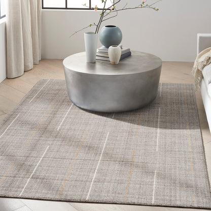 Round concrete-look coffee table with blue and white vases and books on a gray plaid rug in a bright modern living room.