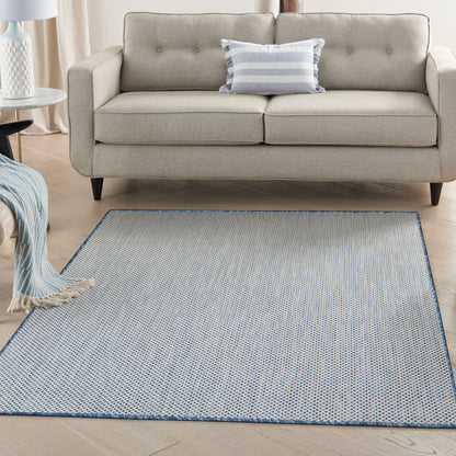 Light blue flat-weave rug (6' x 9') with tiny white dots & a blue border, placed in front of a beige sofa in a bright living room.
