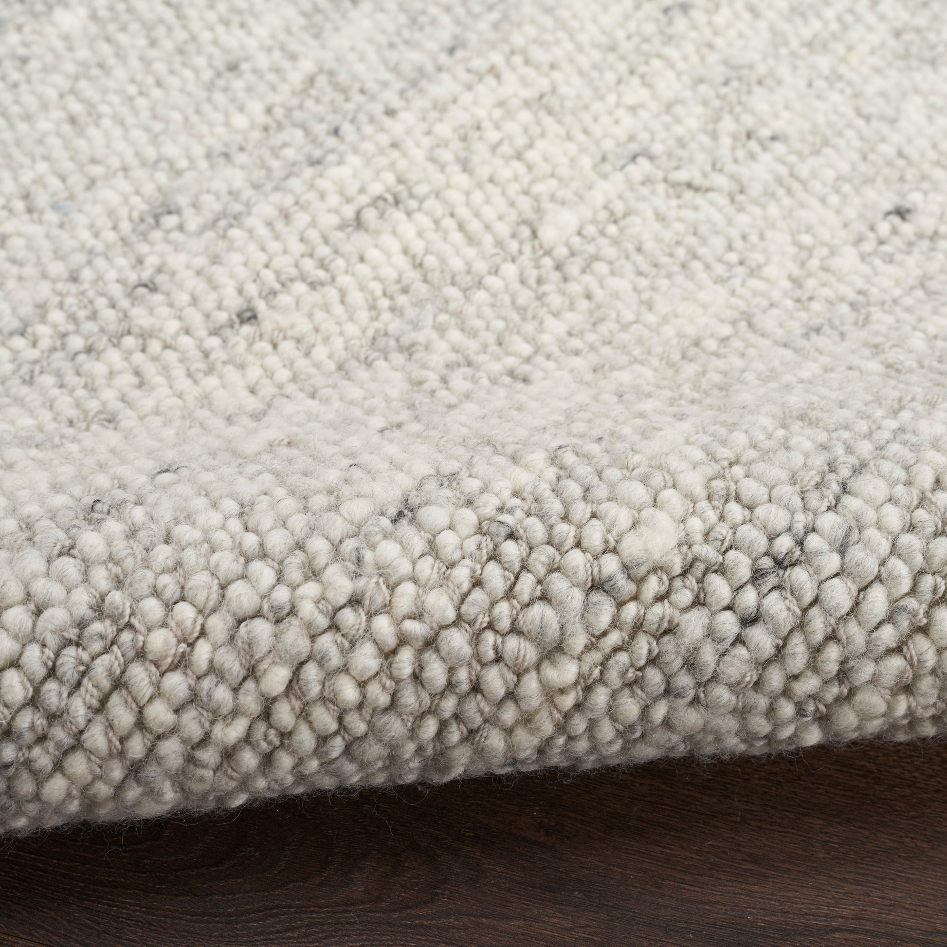 Close-up of a soft boucle rug in light gray and ivory tones with dense loop pile on a dark wood floor.