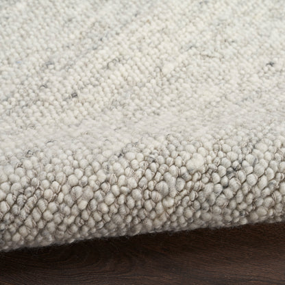 Close-up of a soft boucle rug in light gray and ivory tones with dense loop pile on a dark wood floor.