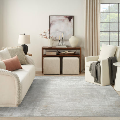Neutral living room with cream sofa, blush pillow, wooden console, framed abstract art, two beige ottomans, light blue rug.
