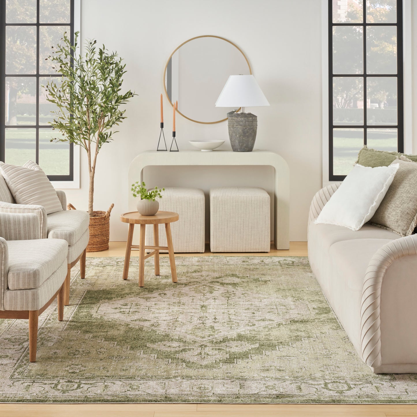 Neutral living room with cream sofas, round mirror, curved cream console, green patterned rug, and wooden round coffee table.