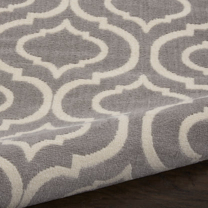 Grey rug with a white quatrefoil lattice pattern on a dark wood floor.
