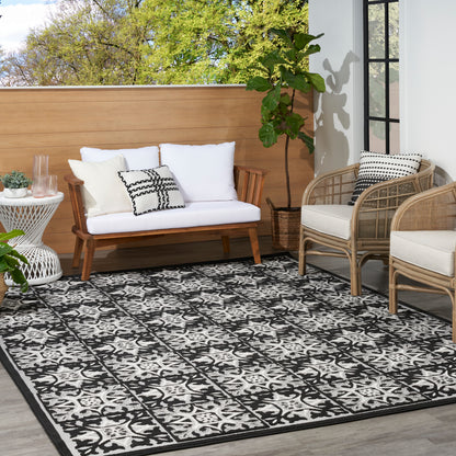 Outdoor patio with white-cushioned wooden sofa, wicker chairs, black-and-white patterned rug, potted plant