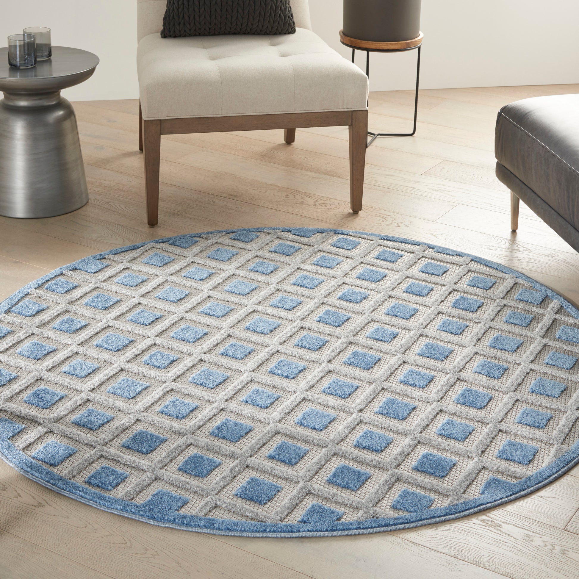 Round beige rug with lattice grid and blue squares, textured flat-weave, in a light-wood living room.