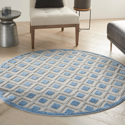 Round beige rug with lattice grid and blue squares, textured flat-weave, in a light-wood living room.