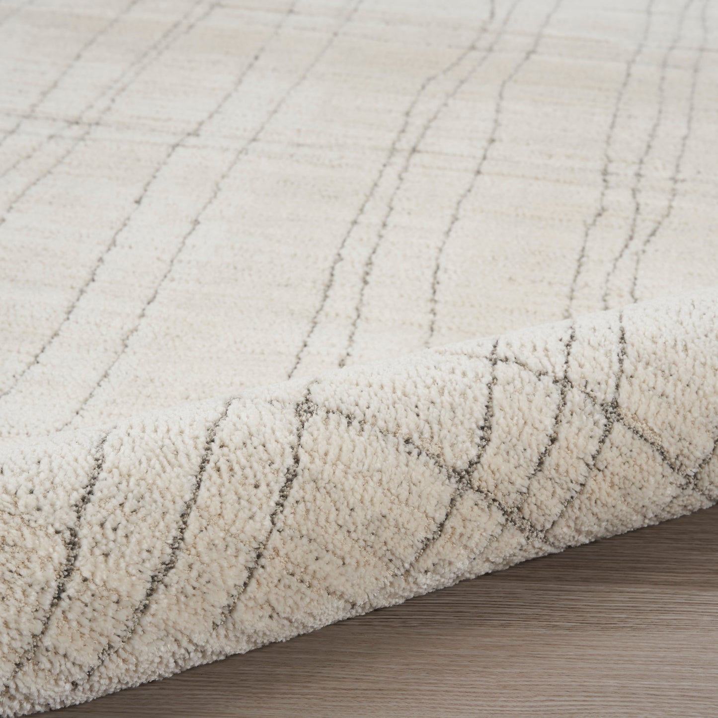 Beige plush area rug with subtle gray diagonal grid lines, rolled edge on wood floor.