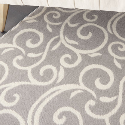 Soft gray rug with white scroll-pattern design; partial beige sofa leg visible.