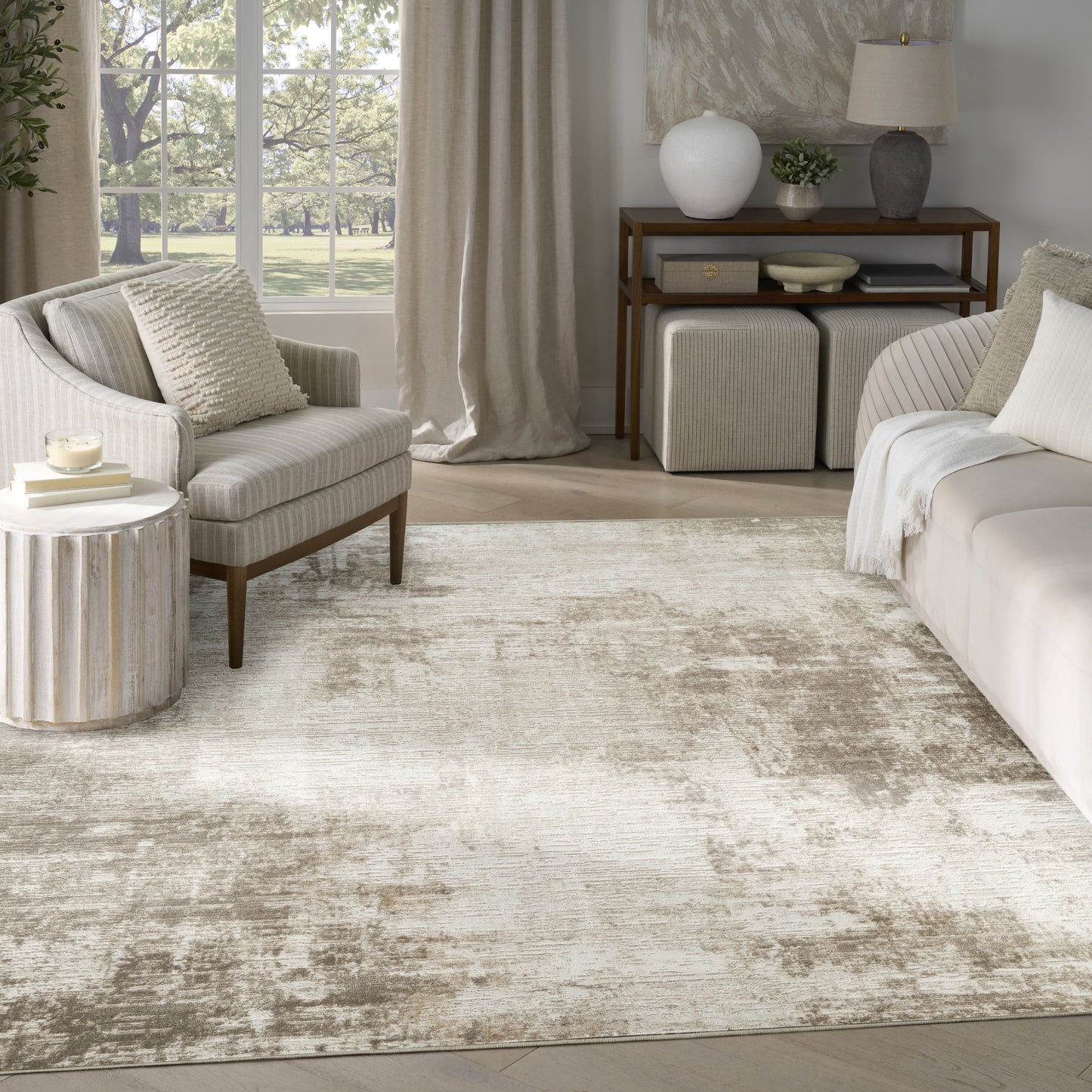 Sunlit neutral living room with beige upholstered sofa and armchair, textured rug, round ribbed side table, and wooden console.