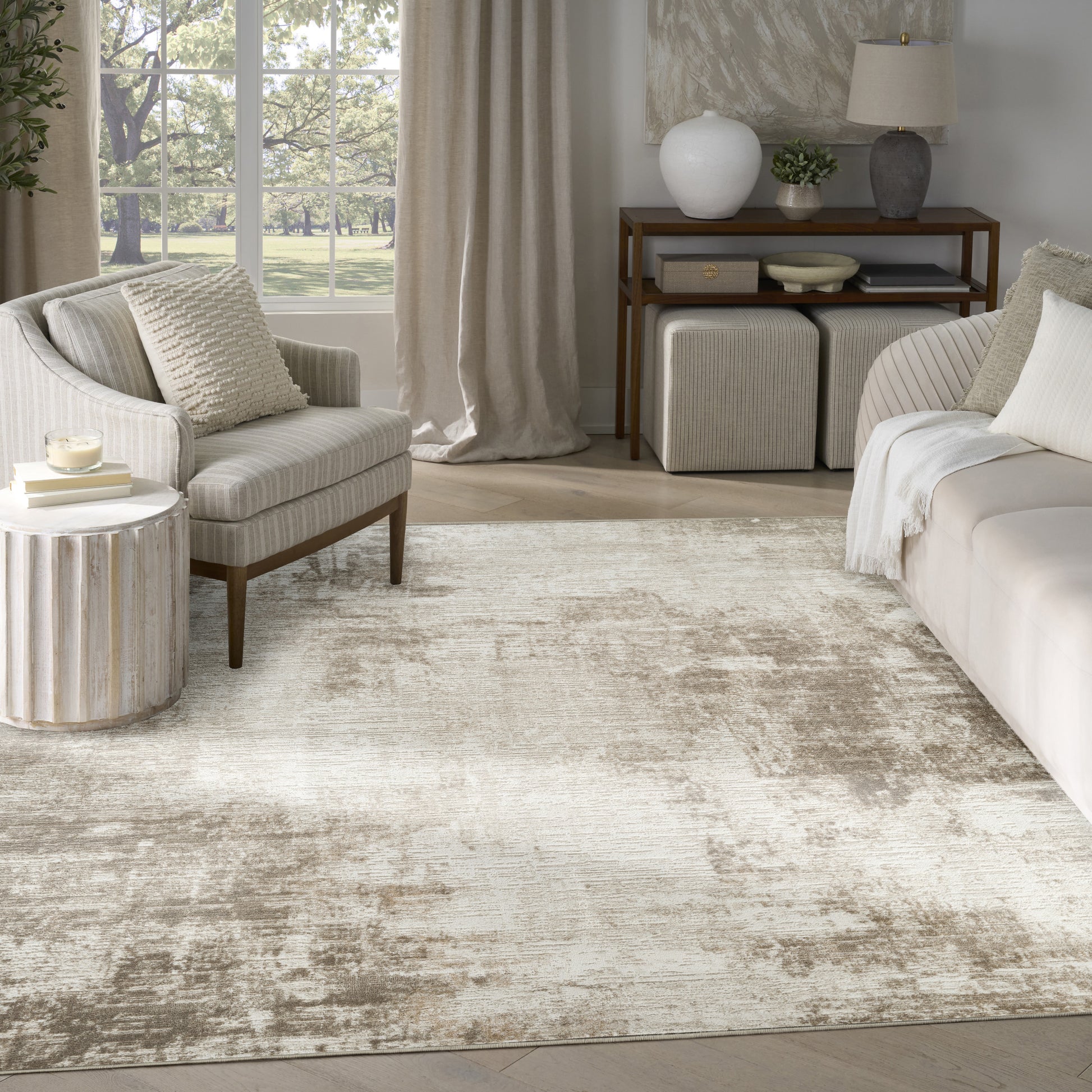 Sunlit neutral living room with beige upholstered sofa and armchair, textured rug, round ribbed side table, and wooden console.