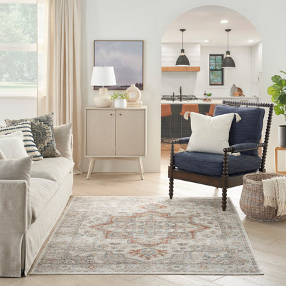 Neutral living room with beige sofa, patterned area rug, light wood cabinet, navy carved-wood armchair, arch to kitchen.