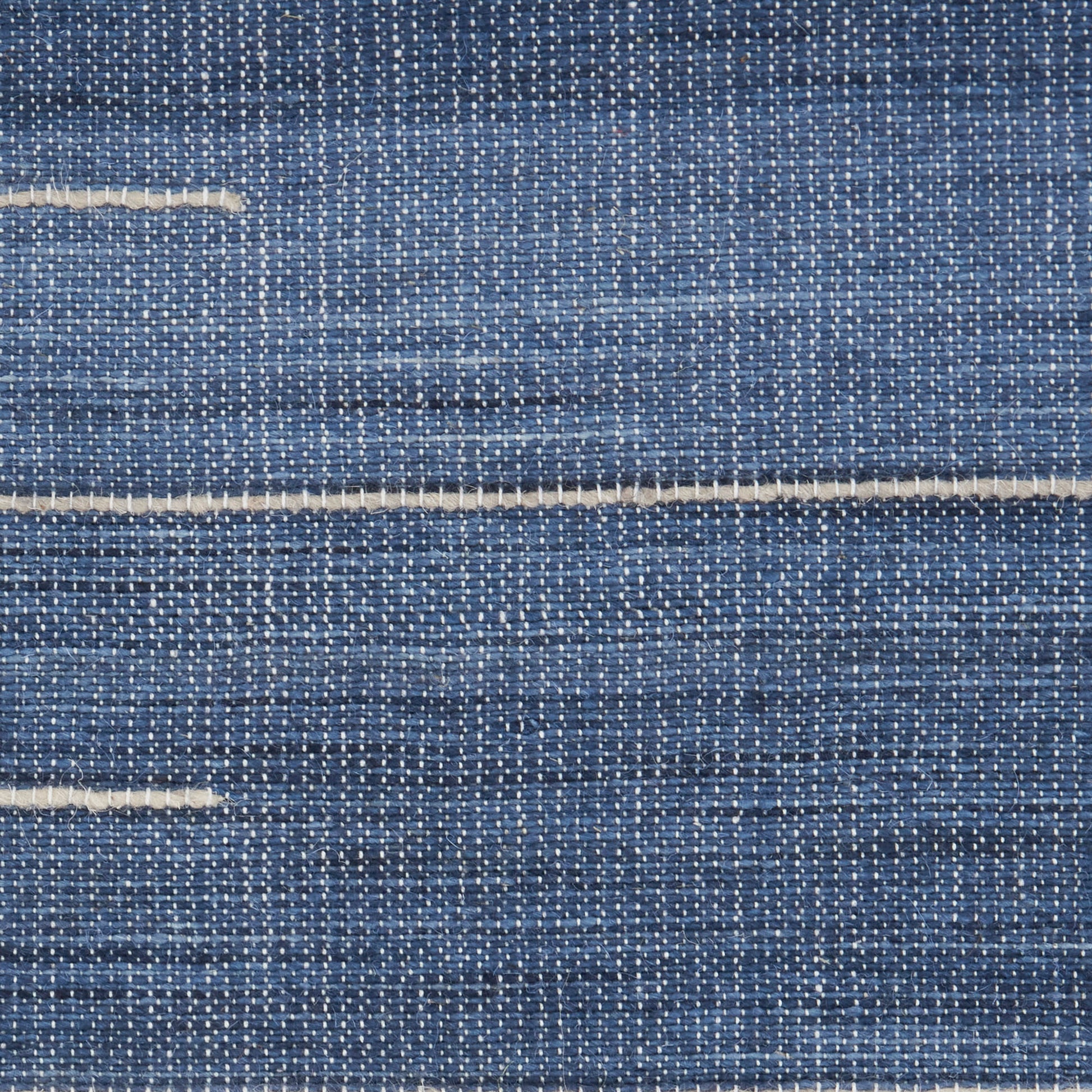 Close-up of blue denim fabric with white weft threads and light horizontal seam lines.