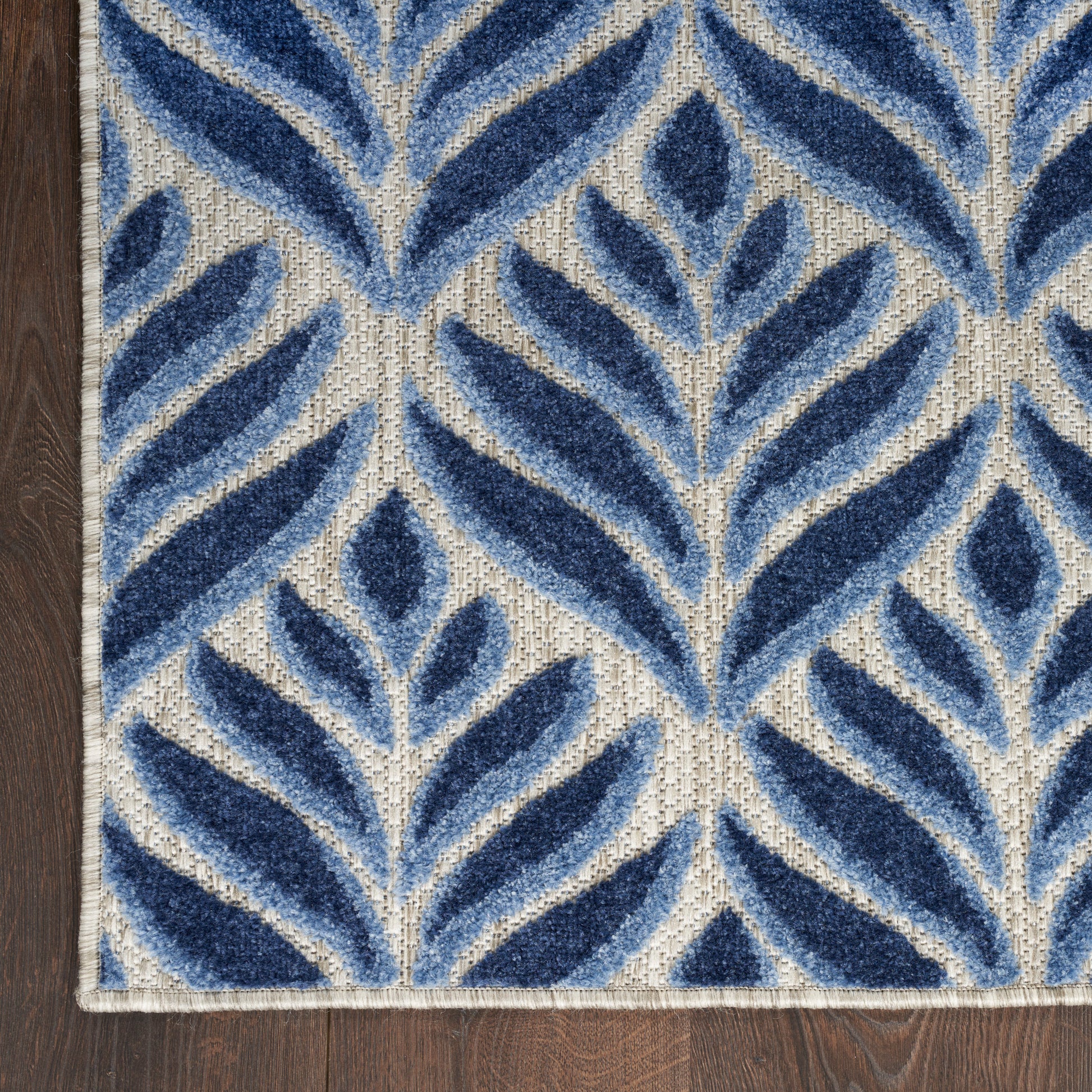 Rectangular blue and ivory leaf-patterned woven rug with navy foliage on beige background.
