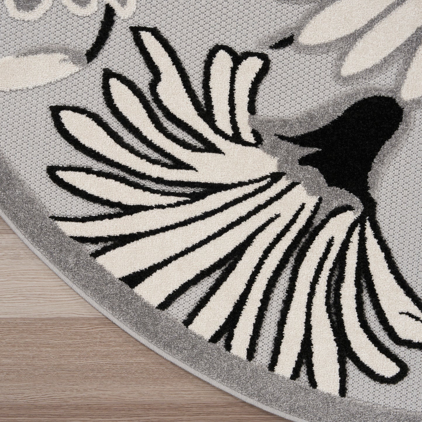 Round gray rug with bold black-and-white floral motif, woven texture and gray border.