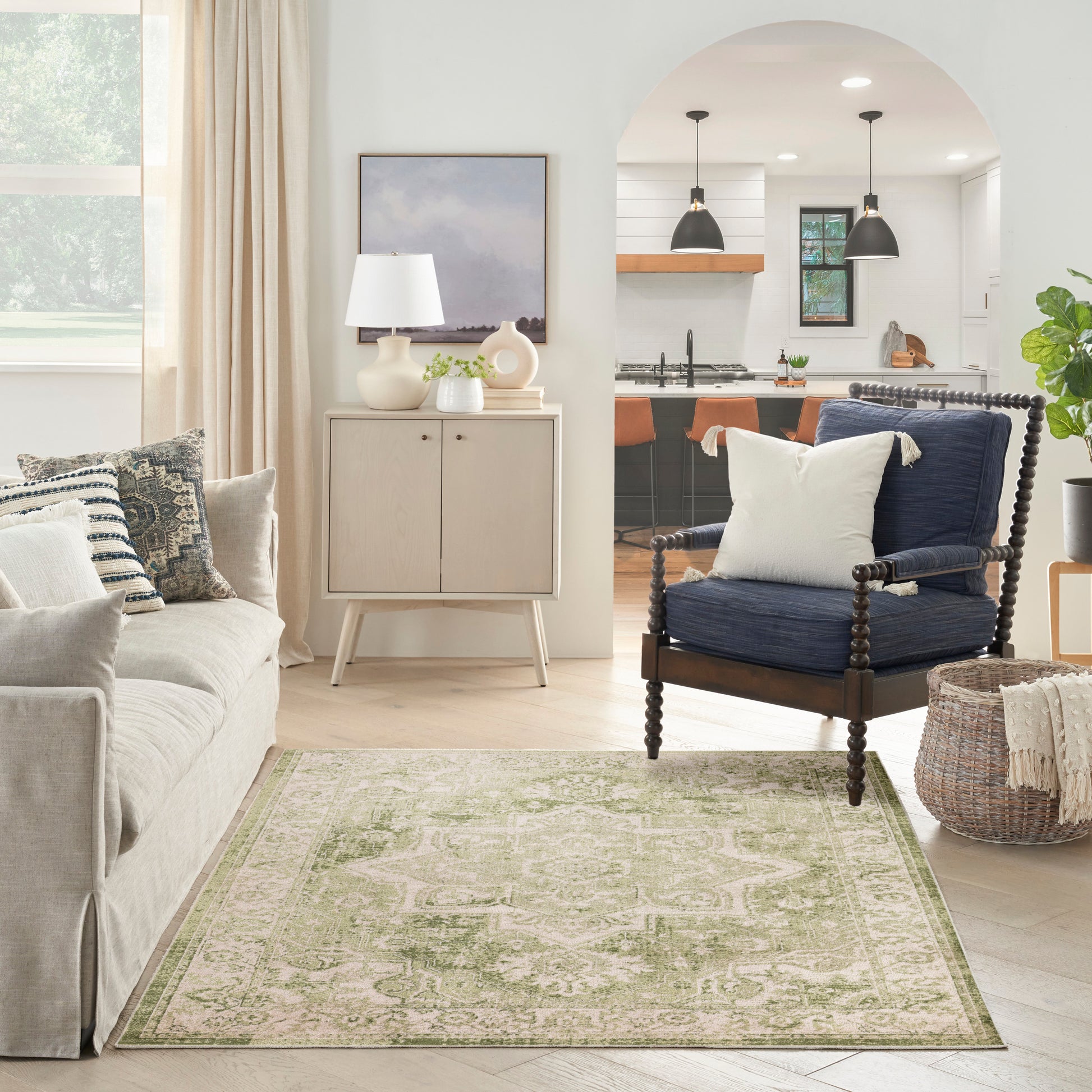 Neutral living room with beige sofa, light wood cabinet, white lamp, green rug, navy spindle-arm chair, and a woven basket.