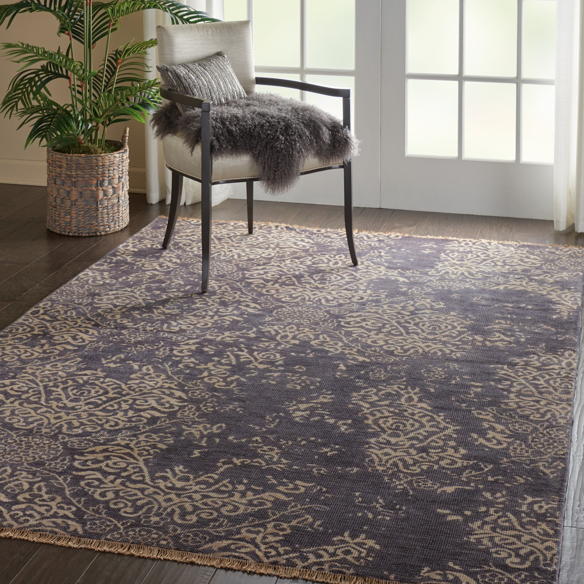 Ornate navy blue & beige area rug with scroll pattern in a living room, paired with a chair and sheepskin throw.