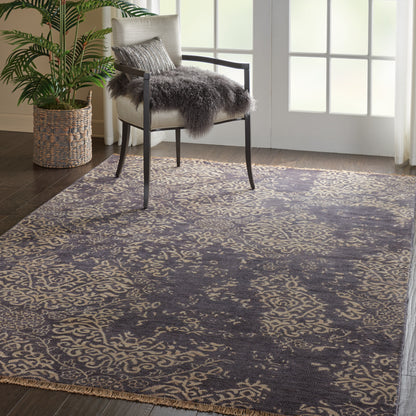 Ornate navy blue & beige area rug with scroll pattern in a living room, paired with a chair and sheepskin throw.