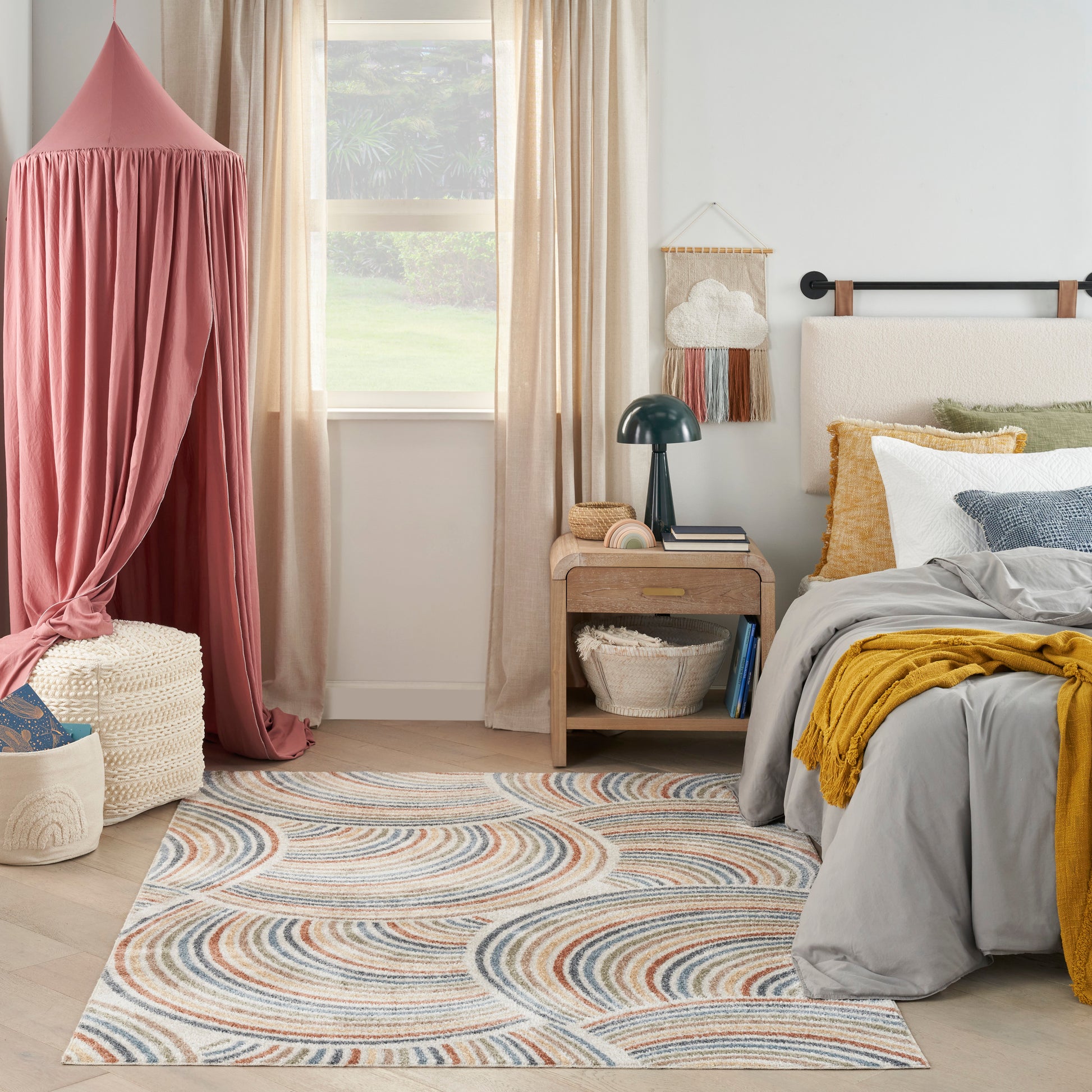 Boho chic bedroom with pink canopy bed, swirl rug in blue/beige, gray bedding, mustard throw, wicker basket, nightstand.